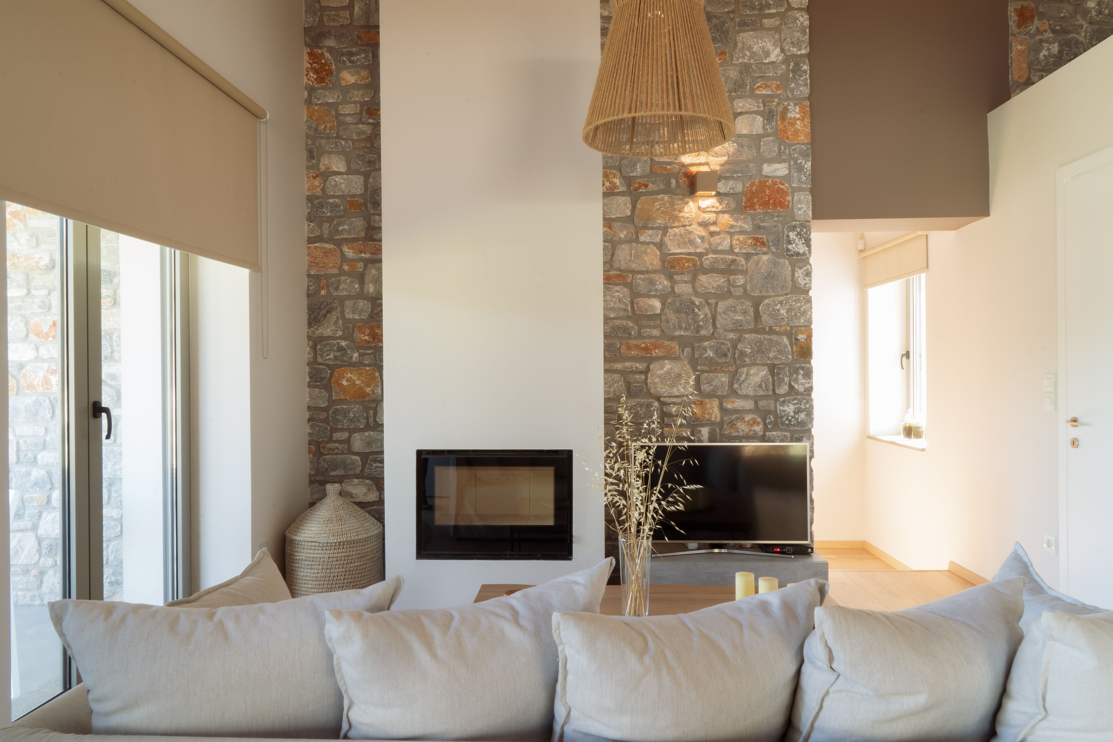A living room with a stone wall, a flat-screen TV, a sofa, and a hanging light fixture.