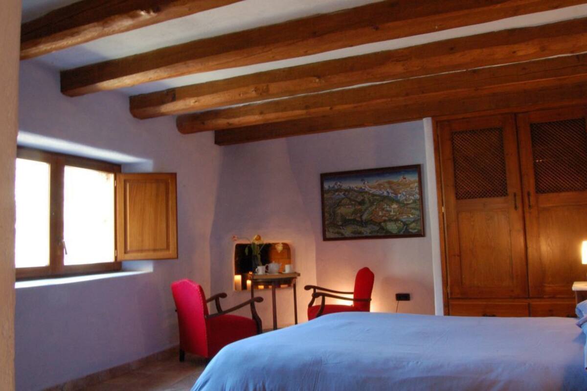Un dormitorio con cama, vigas de techo de madera, una ventana, un cuadro y un armario.