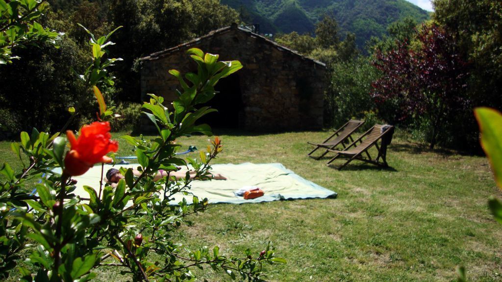 A rustic stone building with a grassy yard, a picnic blanket, and two wooden chairs.
