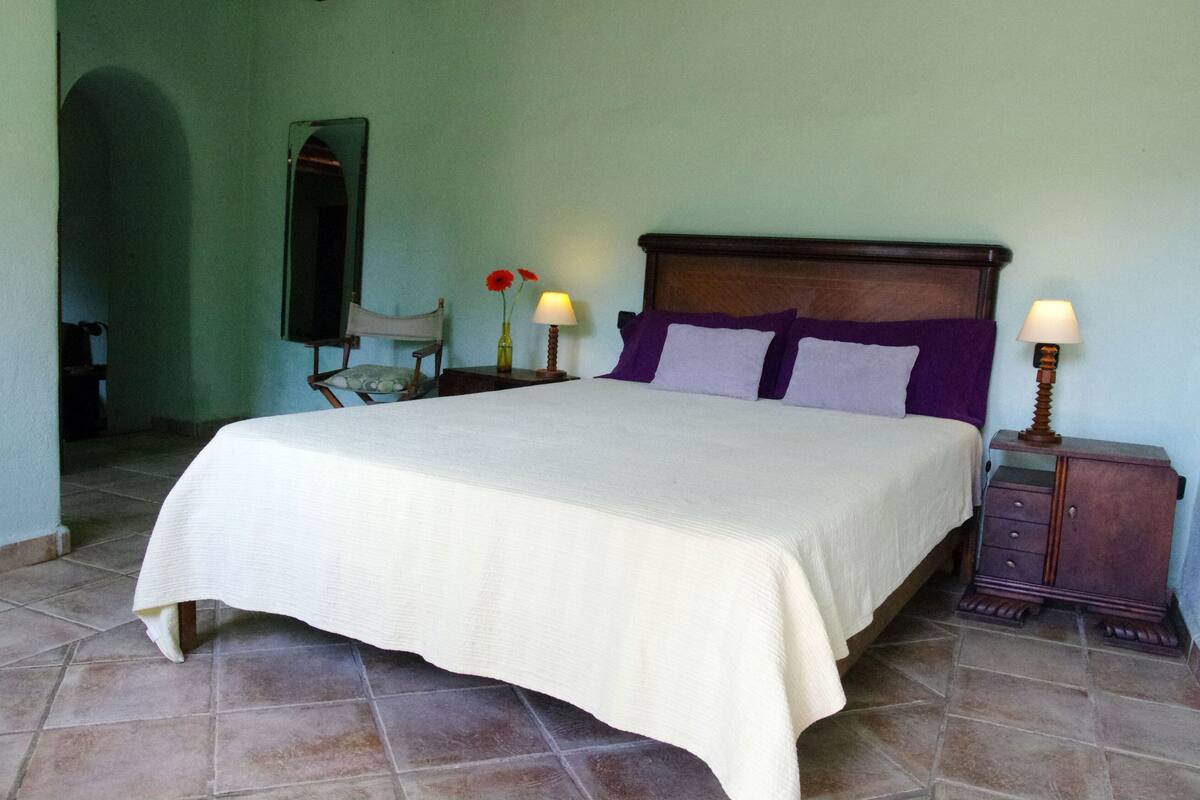 Una cama bien tendida con una colcha blanca, un cabecero de madera y dos lámparas de noche.