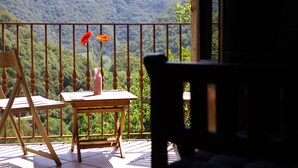 Un balcón con mesa y sillas, con vista a una cadena montañosa boscosa.