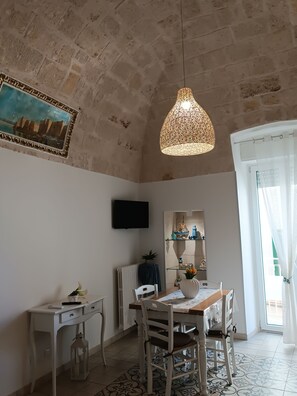 Un coin repas comprenant une table, des chaises, un luminaire suspendu, un tableau et une fenêtre avec des rideaux.