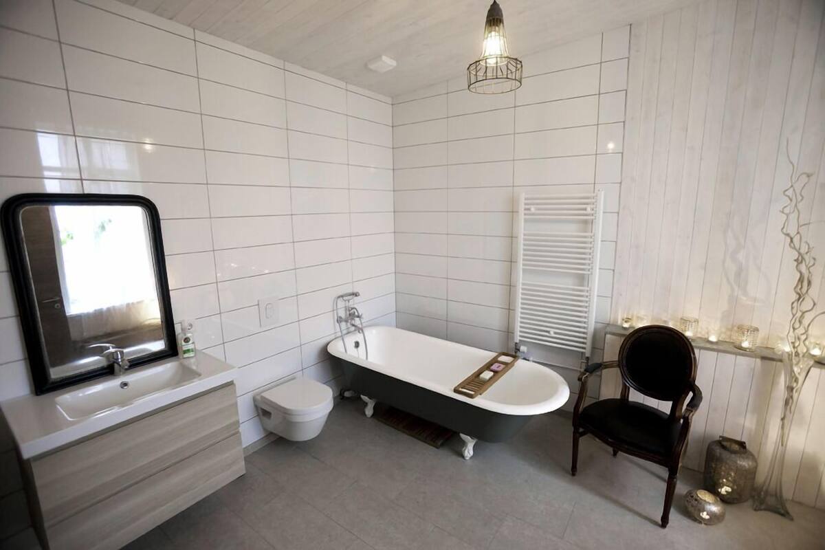 A modern bathroom with a freestanding bathtub, a vanity with a mirror, and a chair.