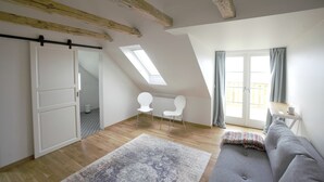 Ein geräumiges Schlafzimmer im Loft-Stil mit Dachfenster, einer Schiebetür, einem grauen Sofa und einem kleinen Tisch am Fenster.