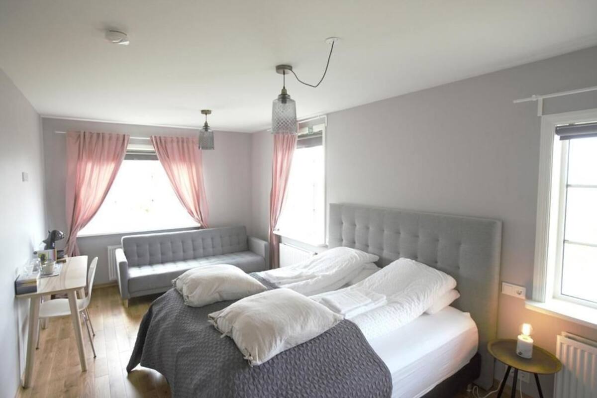 A bedroom with a bed, a desk, and a chair. There are curtains on the windows.