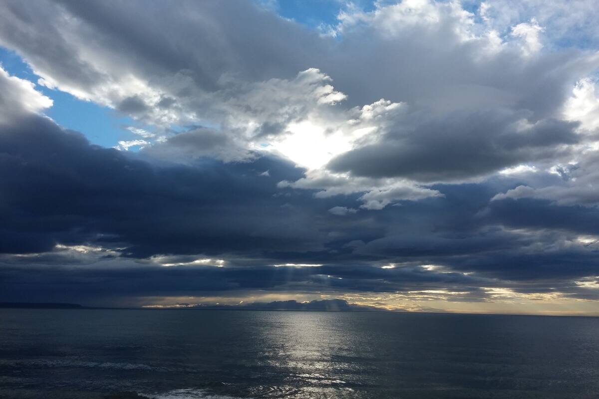 A view of the ocean with a cloudy sky and sunlight breaking through.