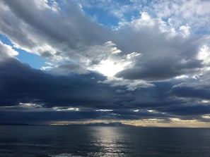 Une vue sur l’océan, avec un ciel nuageux et des rayons de soleil perçant à travers les nuages.