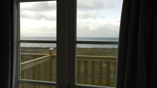 Blick von einem Zimmer mit Holzterrasse auf Strand und Meer.