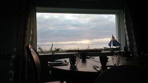 Ein Esstisch mit Blick auf den Sonnenuntergang über dem Wasser, ein Segelboot und ein dekoratives Segelbrett auf der Fensterbank.