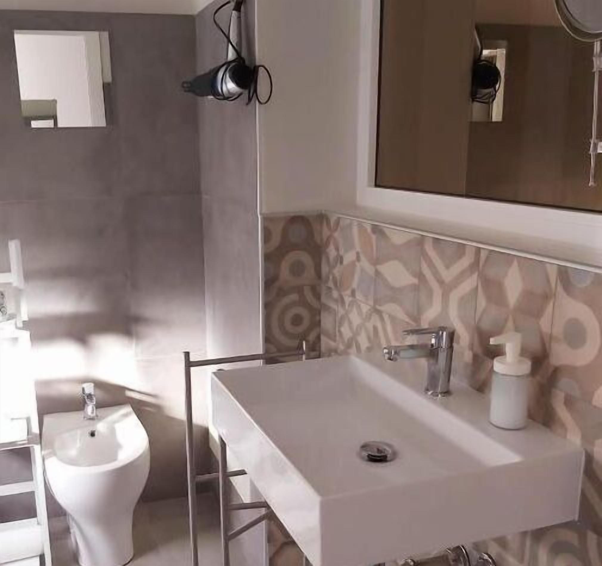 A bathroom with a white sink, a bidet, a mirror, and patterned tiles.