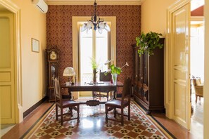 Zona pranzo con tavolo, sedie, lampadario, orologio e mobiletto con una pianta.