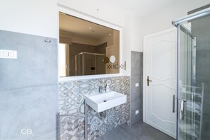 Un bagno moderno con uno specchio grande, un lavandino bianco e una zona doccia.