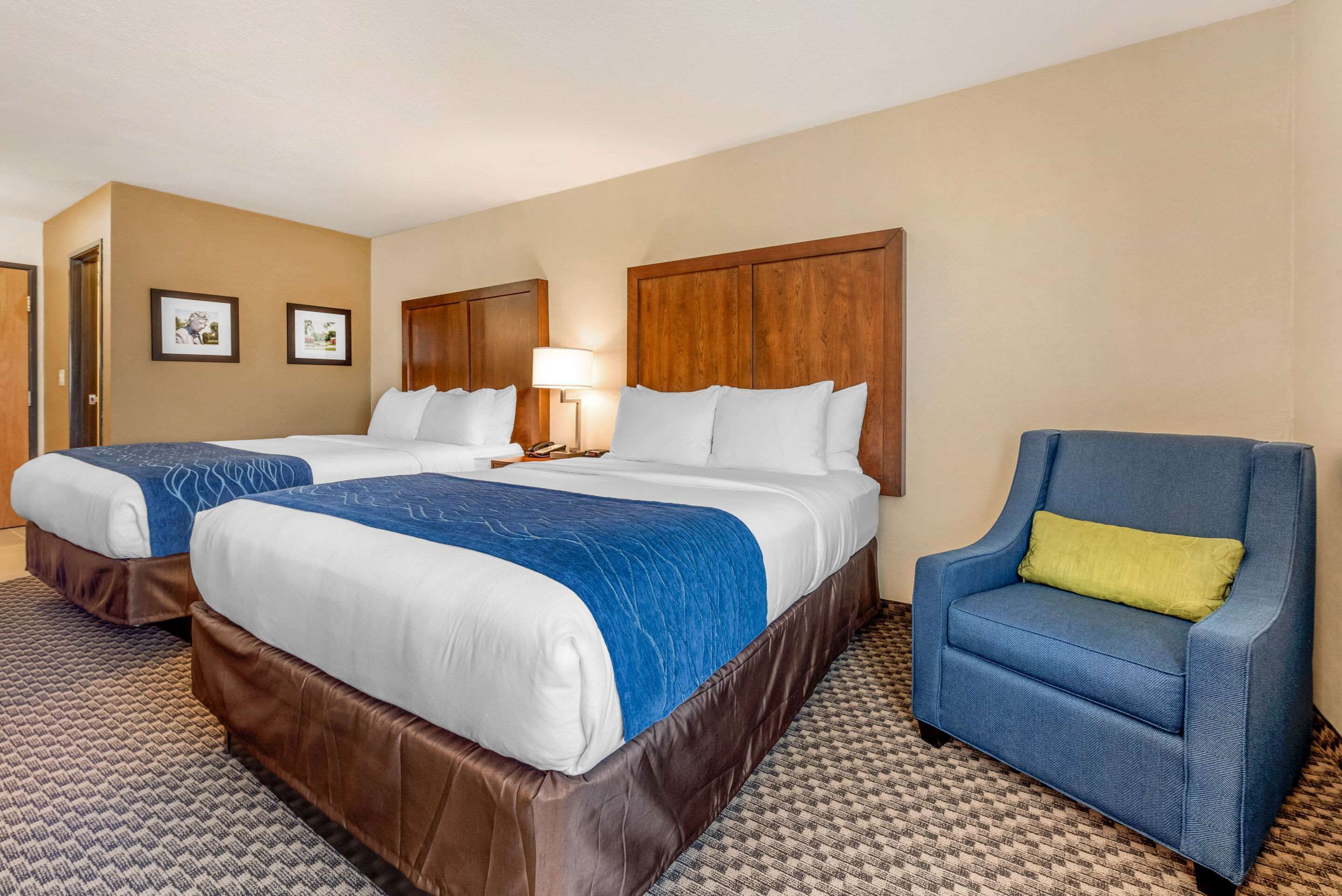 A hotel room with two beds, a blue armchair, and a patterned carpet.
