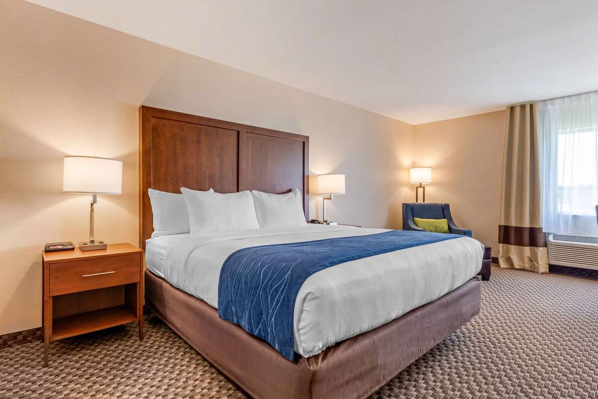 A hotel room with a large bed, two bedside tables with lamps, a chair, and a window with curtains.