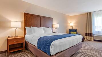 Quarto de hotel com uma cama grande, duas mesas de cabeceira com abajures, uma cadeira e uma janela com cortinas.