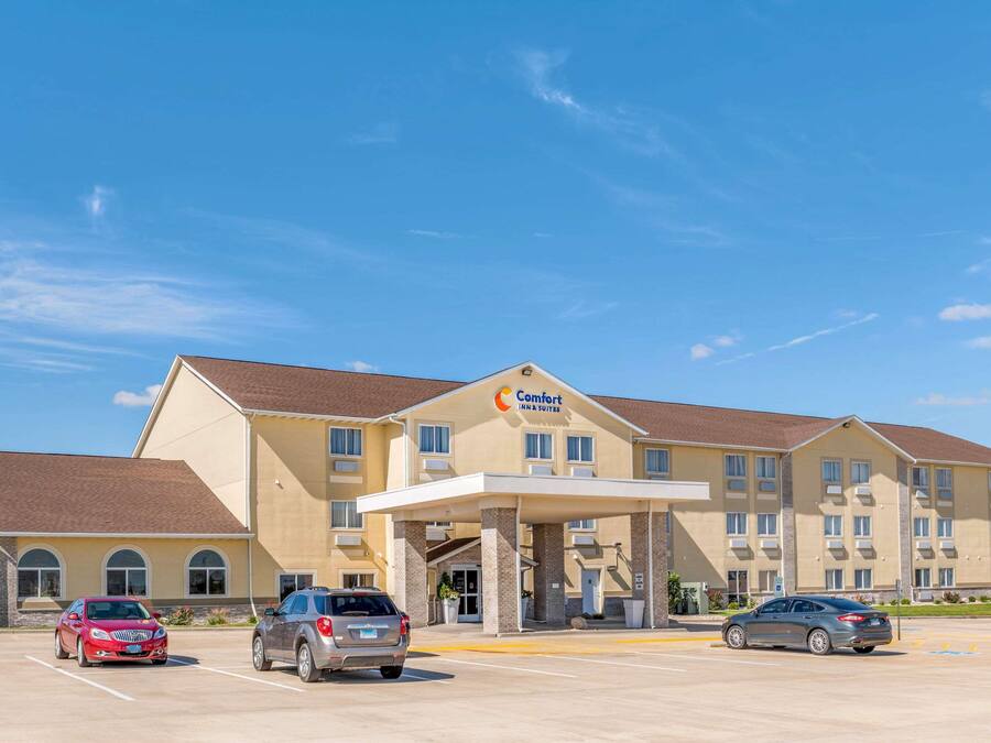 A Comfort Inn & Suites hotel with a parking lot, multiple cars, and a clear blue sky.
