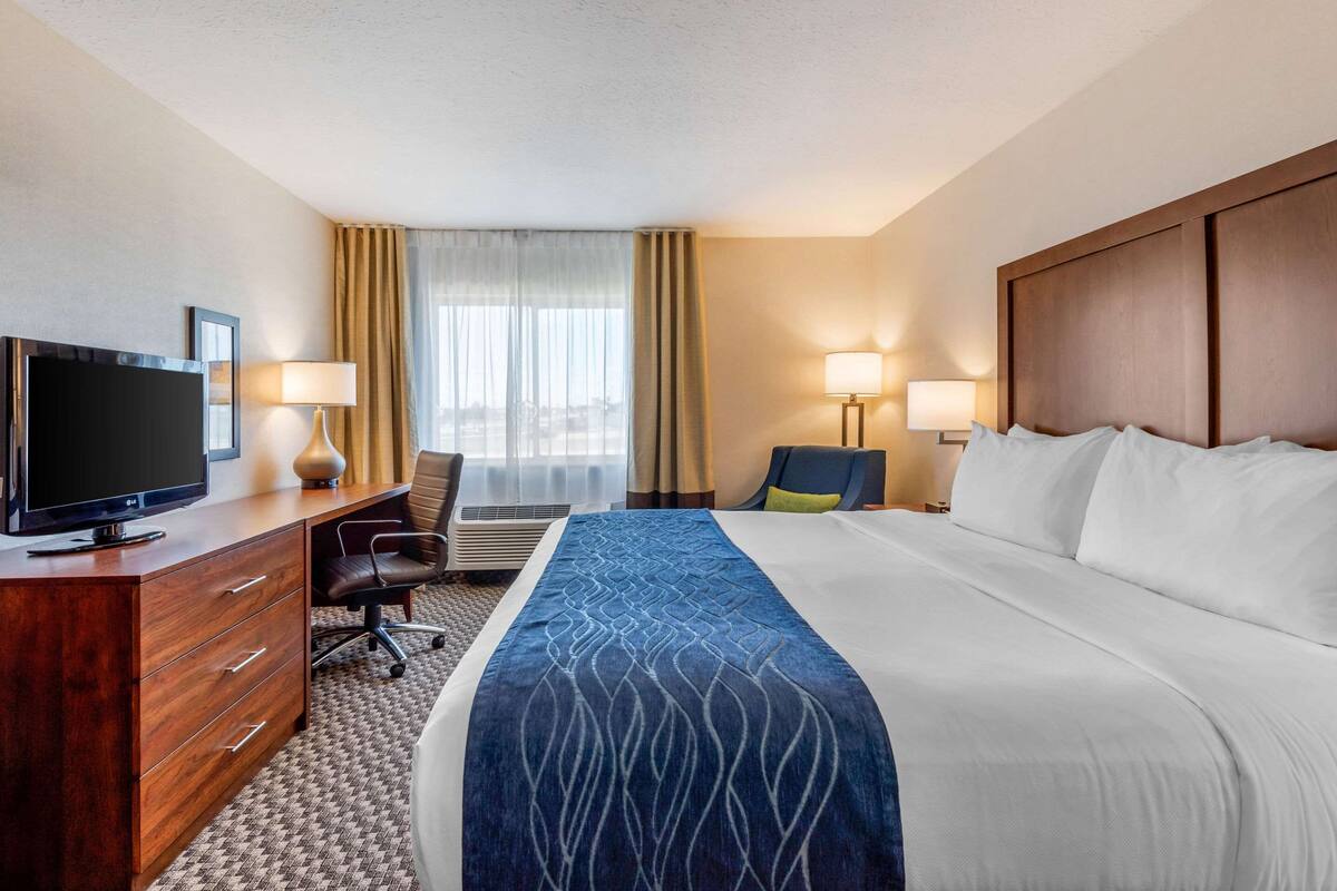A hotel room with a large bed, a desk with a television, two lamps, and a view of the city through the window.