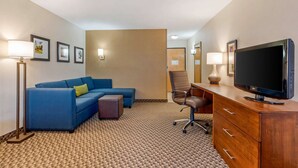 A hotel room with a blue sofa, a wooden dresser with a TV, and framed pictures on the wall. - Comfort Inn & Suites near Route 66 (Lincoln)