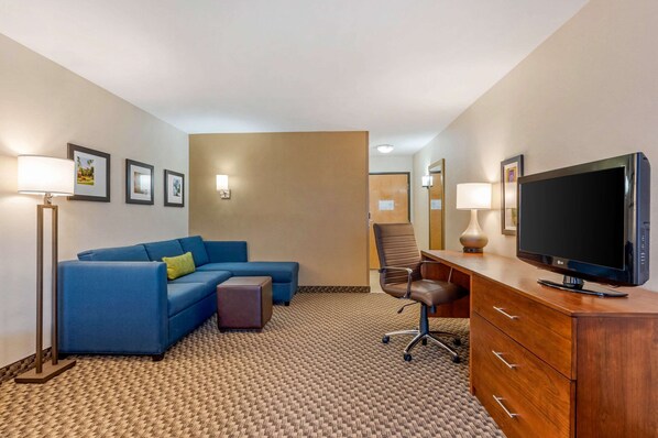 Una habitación de hotel con un sofá azul, un aparador de madera con televisión y cuadros en la pared.