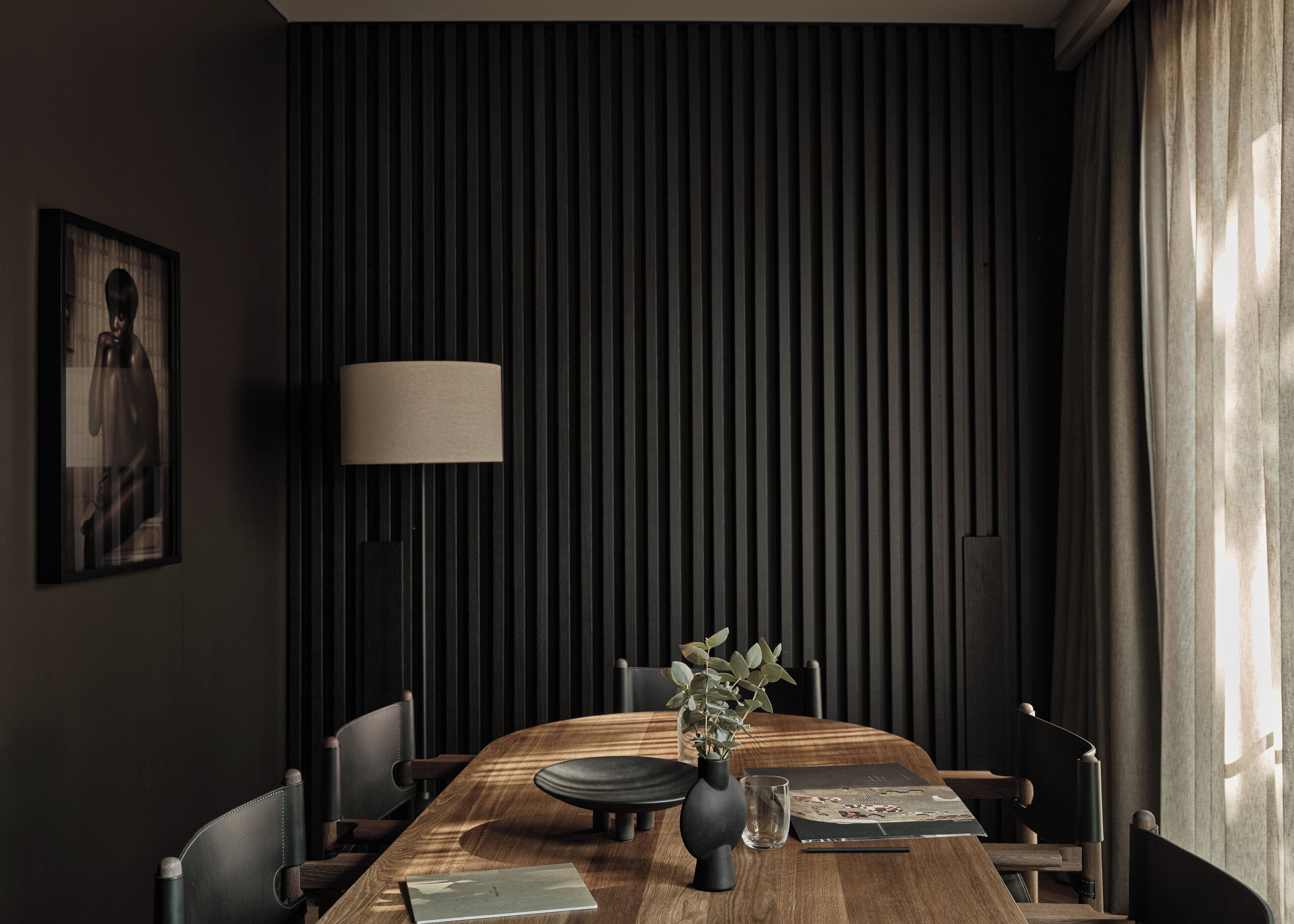 Ein Essbereich mit einem Holztisch, Stühlen, einer Vase mit Pflanzen, einer Lampe und einem gerahmten Bild an der Wand.