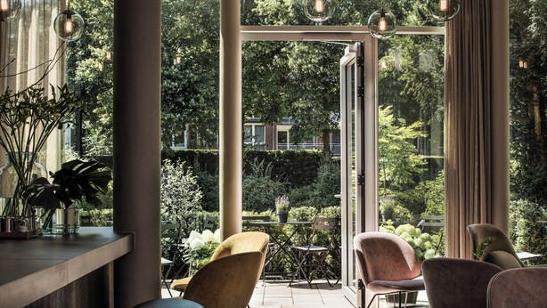 Een modern buitenzitgedeelte met stoelen en een tafel, met uitzicht op een weelderige tuin en een gebouw op de achtergrond.