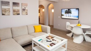 A modern living room with a sofa, coffee table, and a dining area with chairs and a TV. - Cozy Penthouse - Stunning View Acropolis (Athens)