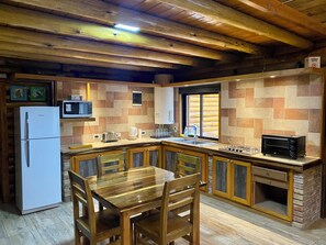 A kitchen with a wooden table, chairs, a refrigerator, a microwave, a toaster, and a built-in oven.