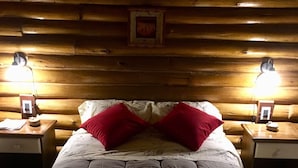 A cozy log cabin bedroom with a large bed, two bedside lamps, and a framed picture on the wall. - Cabaña La Emilia (Uspallata)