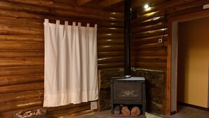 A log cabin interior with a wood-burning stove, a curtain, and a crate of firewood. - Cabaña La Emilia (Uspallata)