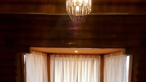 A log cabin room with a large window, wooden walls, and a chandelier. - Cabaña La Emilia (Uspallata)