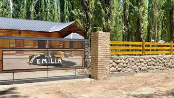 Una cabaña de madera con techo de metal, rodeada por un muro de piedra y una valla de madera.