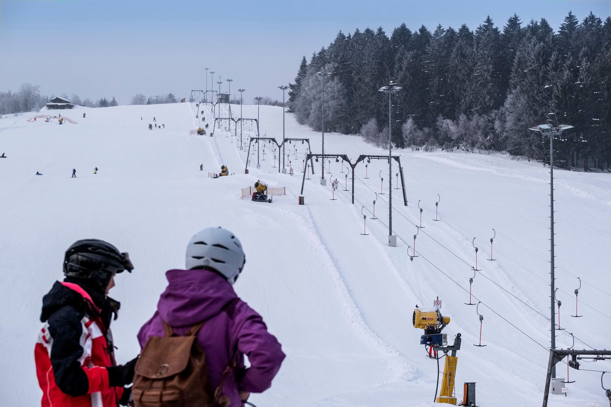 Une piste de ski avec un télésiège, des arbres et un ciel dégagé.