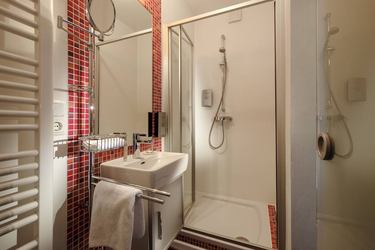 Ein modernes Badezimmer mit einer gläsernen Duschkabine, einem weißen Waschbecken und einem Handtuchhalter.