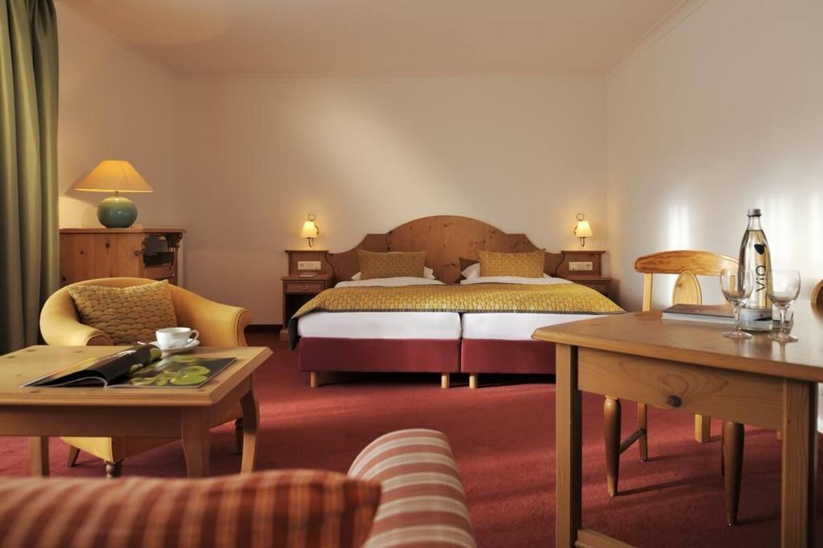 Ein Hotelzimmer mit einem Doppelbett, zwei Nachttischen mit Lampen, einem Holztisch, einem Stuhl und einem Sofa.