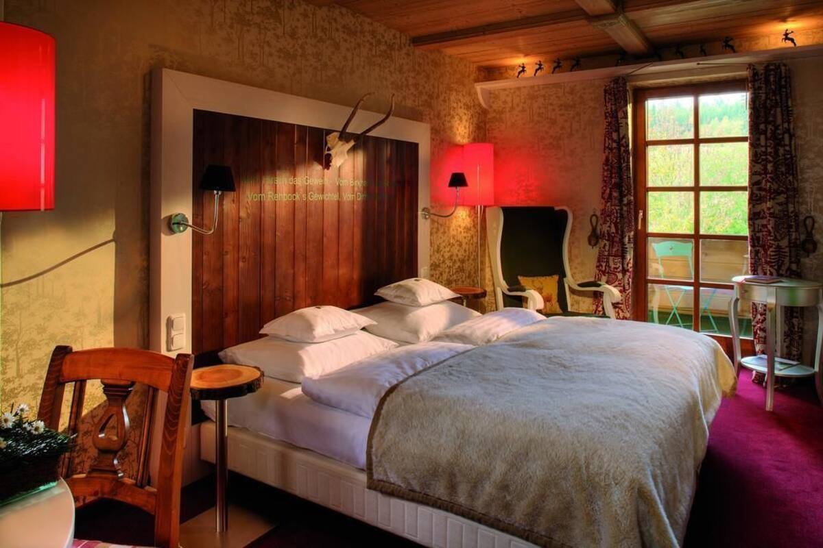 Ein Schlafzimmer mit einem hölzernen Kopfteil, einem Bett mit weißen Bettwäsche, einer roten Lampe und einem Fenster mit gemusterten Vorhängen.