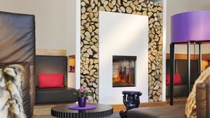 A modern living room with a fireplace, a sofa with red cushions, a round coffee table with a purple vase, and a black side table. - Berghotel Maibrunn (Sankt Englmar)