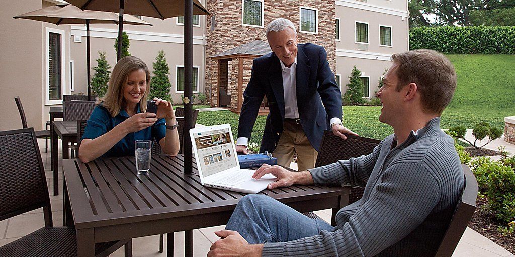 A group of people seated at an outdoor table with a laptop, a glass of water, and a tablet.