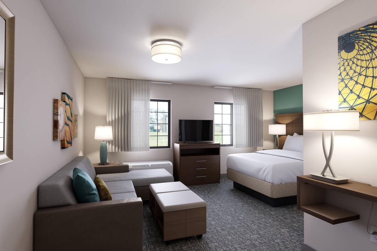 Une chambre d’hôtel avec un canapé, un lit, une télévision et un bureau avec une lampe.