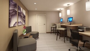 Een moderne hotelkamer met een receptiebalie, twee computermonitoren, een printer en een zithoek met stoelen en een bank.
