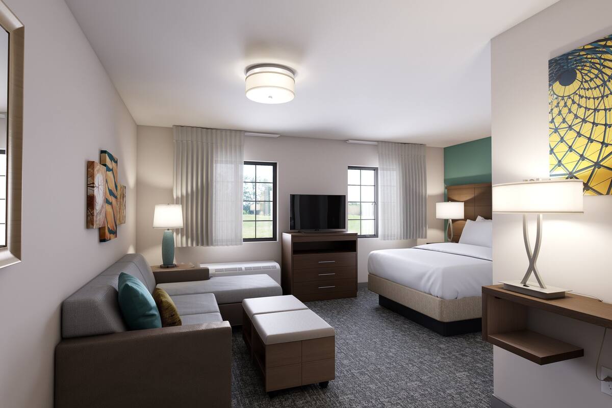 Een hotelkamer met een bank, een bed, een televisie en een bureau met een lamp.