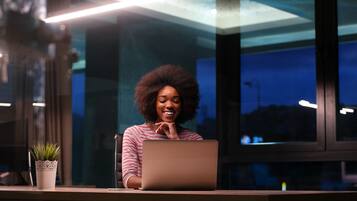 A person sitting at a desk with a laptop, a potted plant, and a window with a view of the night sky.