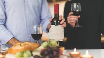 Una mesa con una botella de vino, copas, pan, uvas y velas.