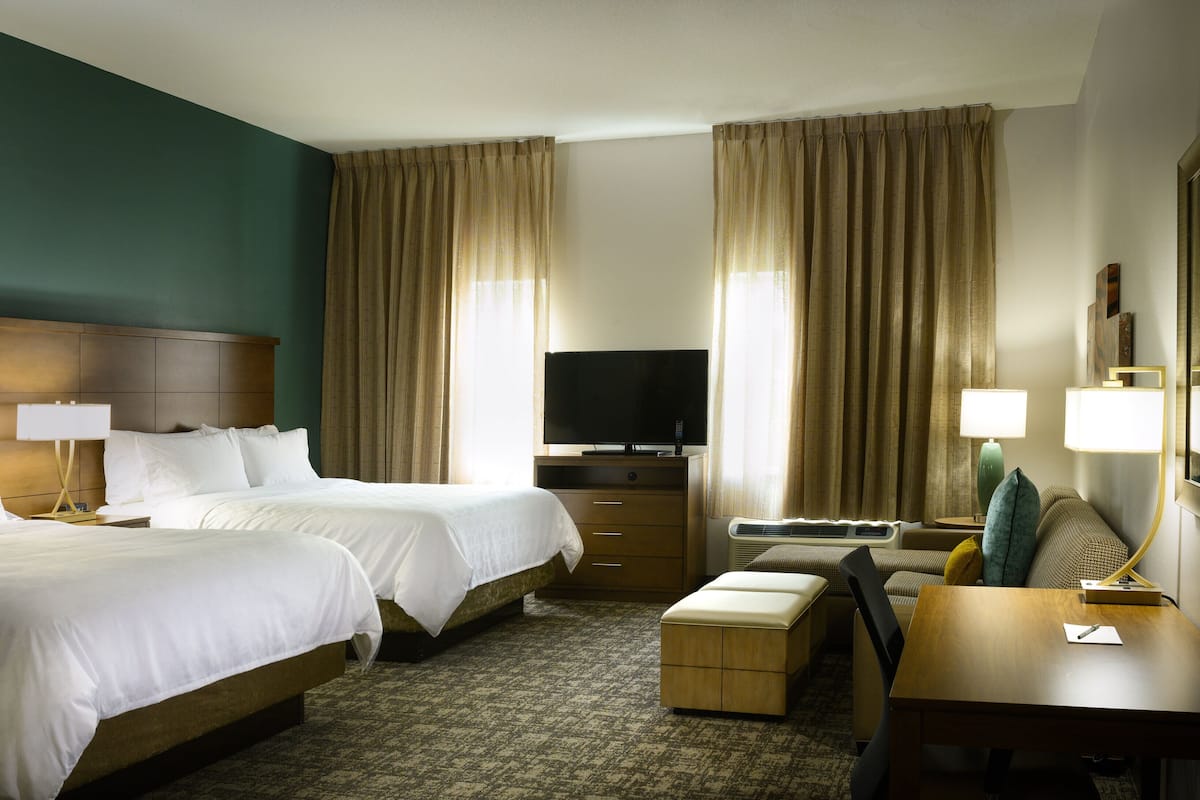 Een hotelkamer met twee bedden, een bureau, een televisietoestel en een groot raam met gordijnen.