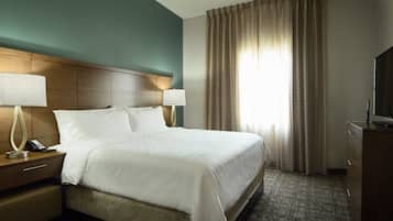 A hotel room with a large bed, two bedside tables with lamps, a television, and a window with curtains.
