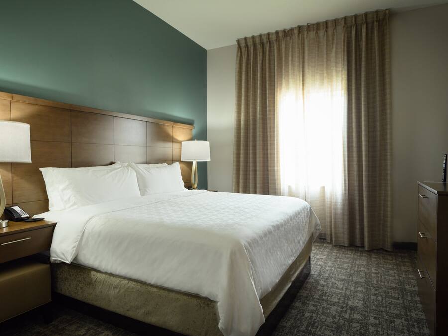 A hotel room with a large bed, two bedside tables with lamps, a television, and a window with curtains.