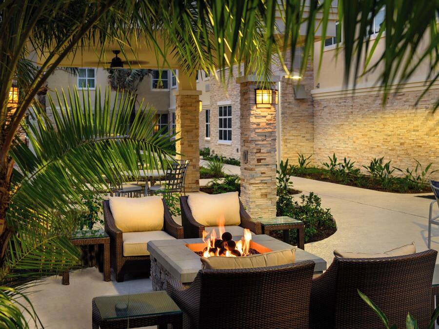 An outdoor seating area with wicker furniture, a fire pit, and palm trees.
