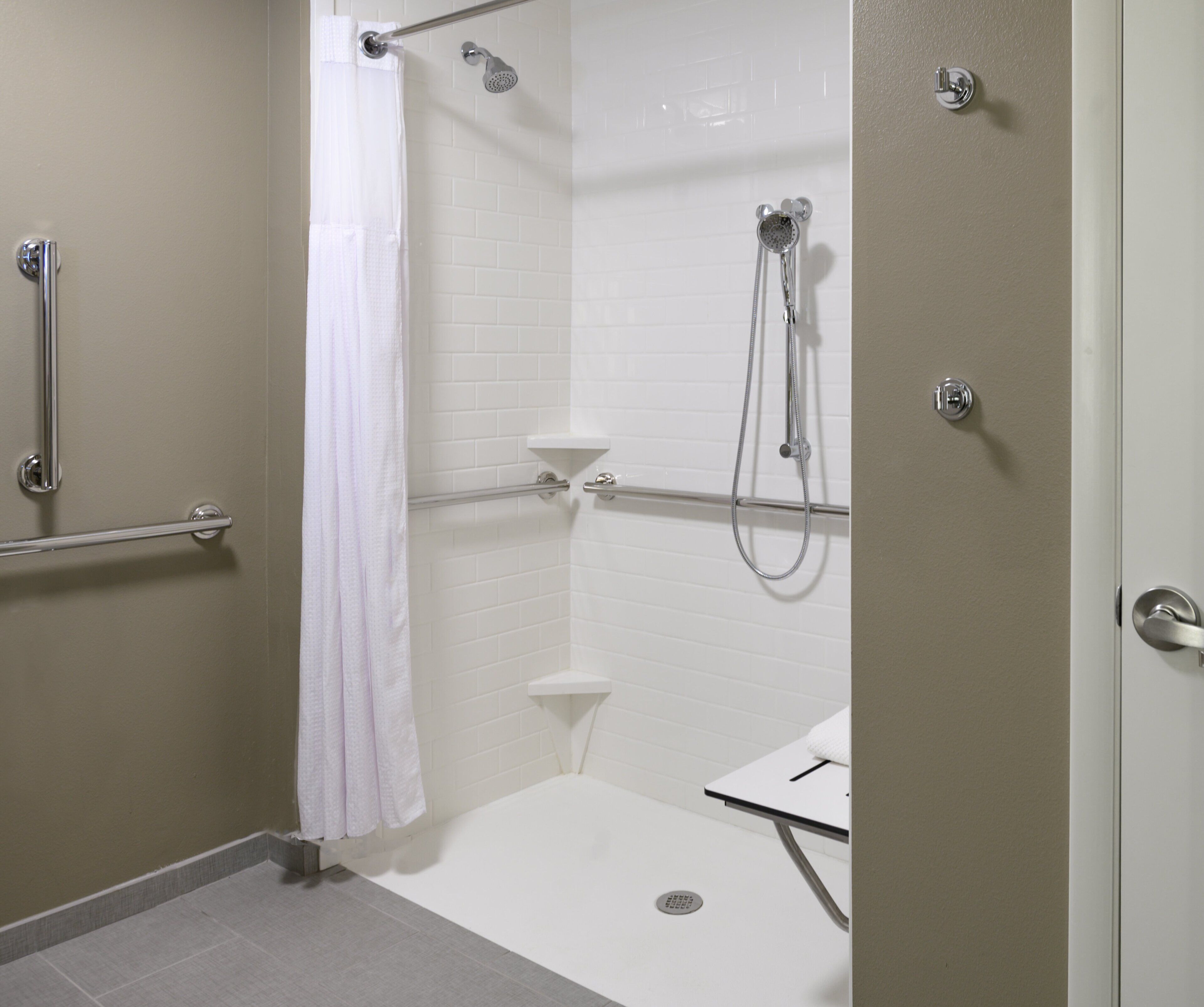 Un baño moderno con cabina de ducha, barras de apoyo, inodoro y lavamanos.