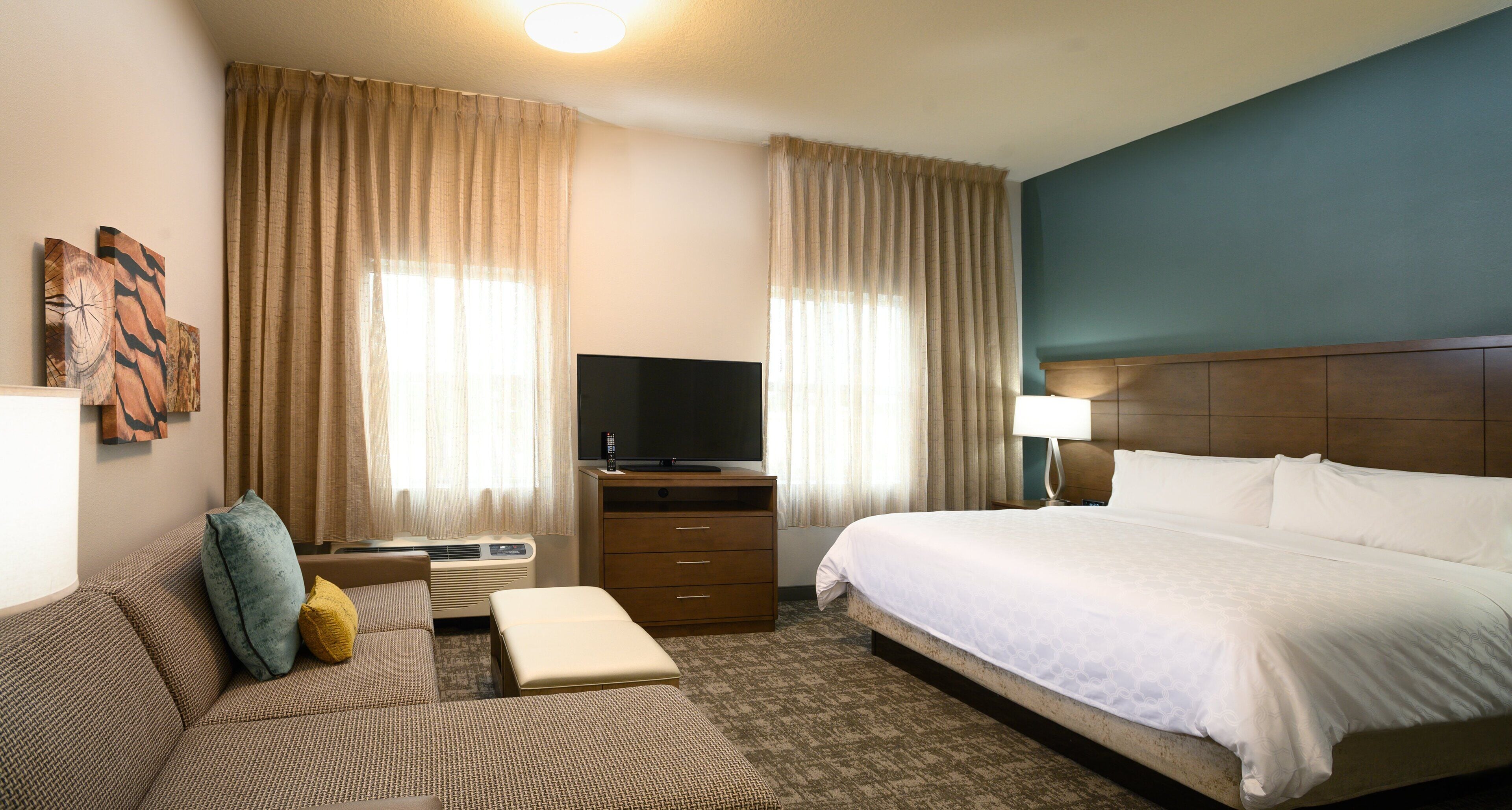 A hotel room with a bed, a sofa, a television, a dresser, and curtains.