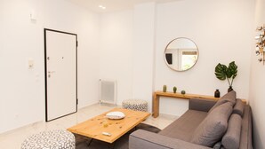 A modern living room with a grey sofa, a wooden coffee table, a patterned ottoman, a round mirror, and a small plant on a shelf. - Luxurious Apartment in Athens Downtown (Athens)