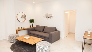 A modern living room with a grey sofa, wooden coffee table, patterned ottomans, a round mirror, and abstract wall art. - Luxurious Apartment in Athens Downtown (Athens)